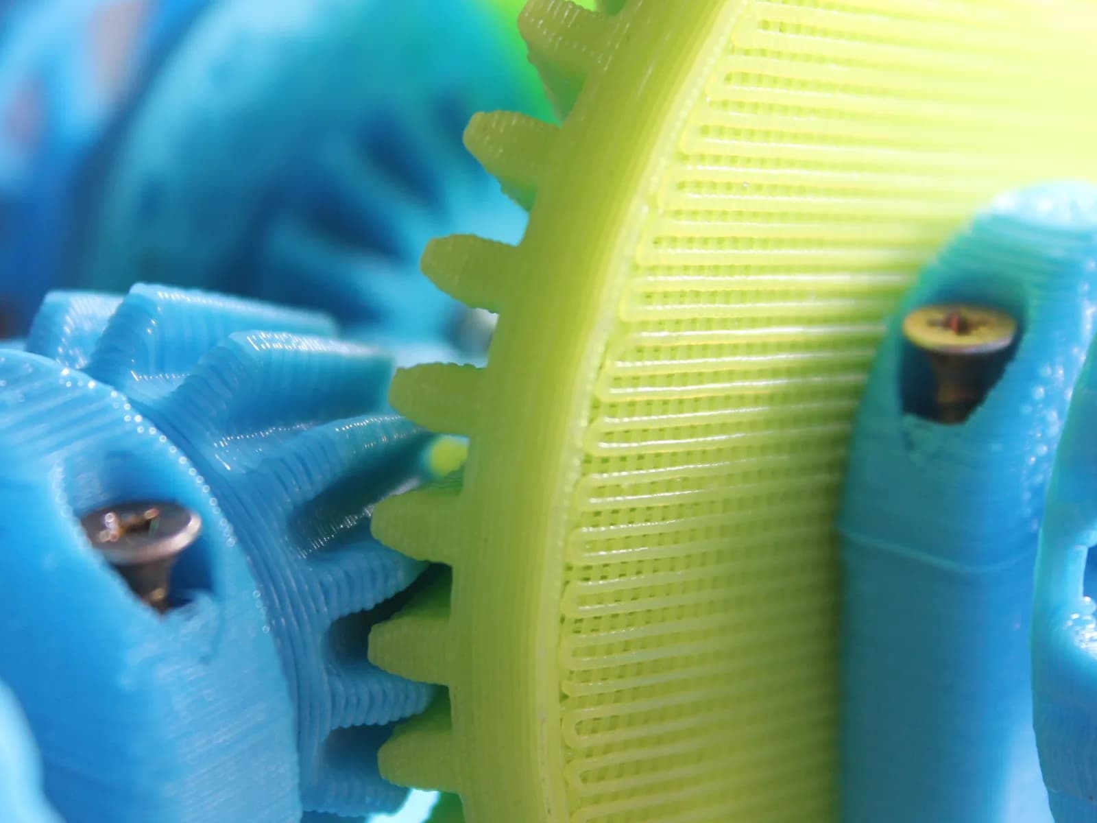 Blue and yellow-green printed plastic gears meshing, with visible layer lines